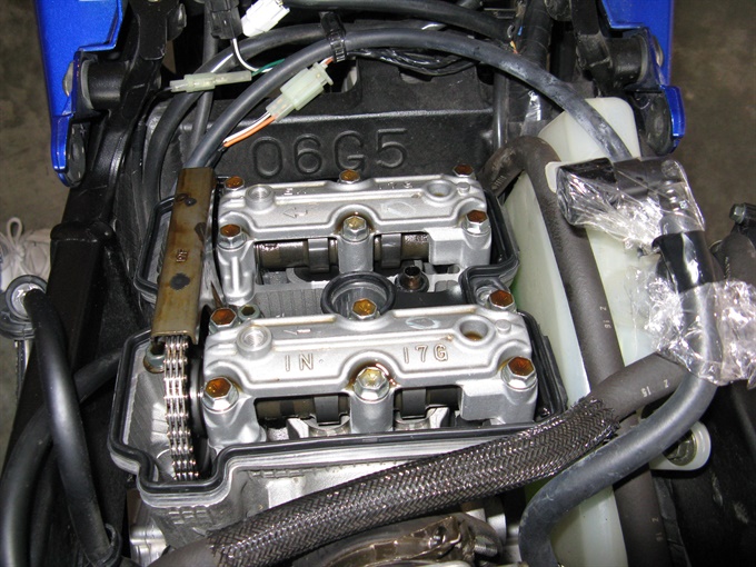 Rear valve cover removed on Suzuki DL650; cam chain, cam shafts and tappets visible.