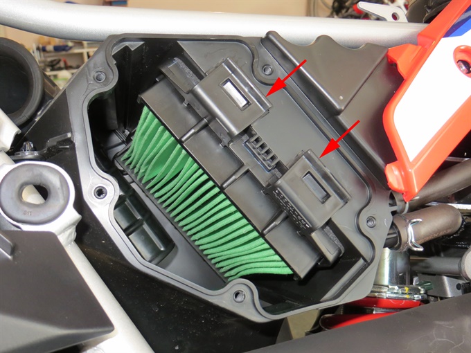 CRF300L air box with air filter installed. Arrows point to tabs/clips to release filter.