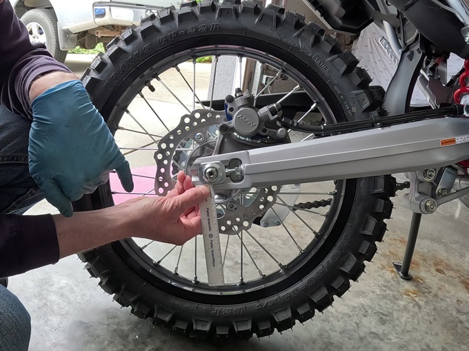 Checking alignment marks on adjuster relative to reference mark (hole) on swingarm - CRF300L