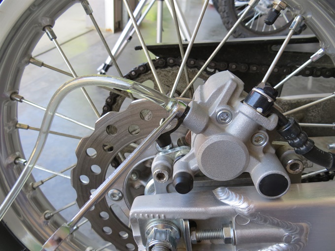 Fresh brake fluid (Prestone DOT 4) visible in bleed tube attached to rear caliper of a KLX140L (to illustrate).